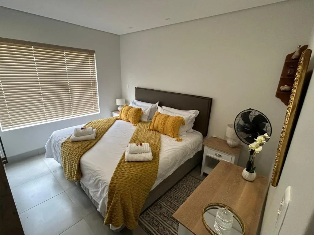 Spacious bedroom with queen bed, golden cushions, fresh towels, and window blinds