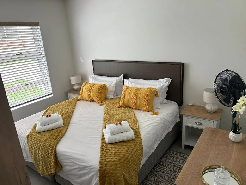 Bright bedroom with queen bed, golden pillows, white linens, and bedside tables