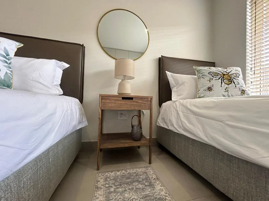Twin beds with neutral bedding, wooden nightstand, and round mirror accent.
