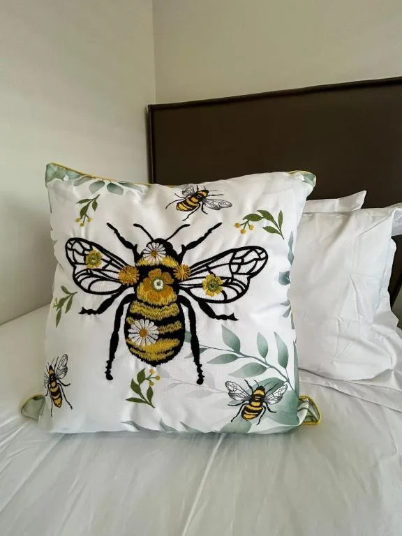 Decorative pillow with embroidered bee and floral botanical design on bed