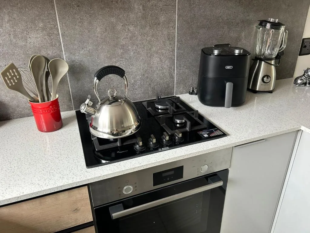 Modern kitchen counter with gas cooktop, kettle, blender, and cooking utensils