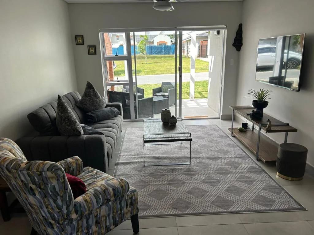 Modern living room with gray sofa, patterned armchair, TV, and glass doors opening to garden