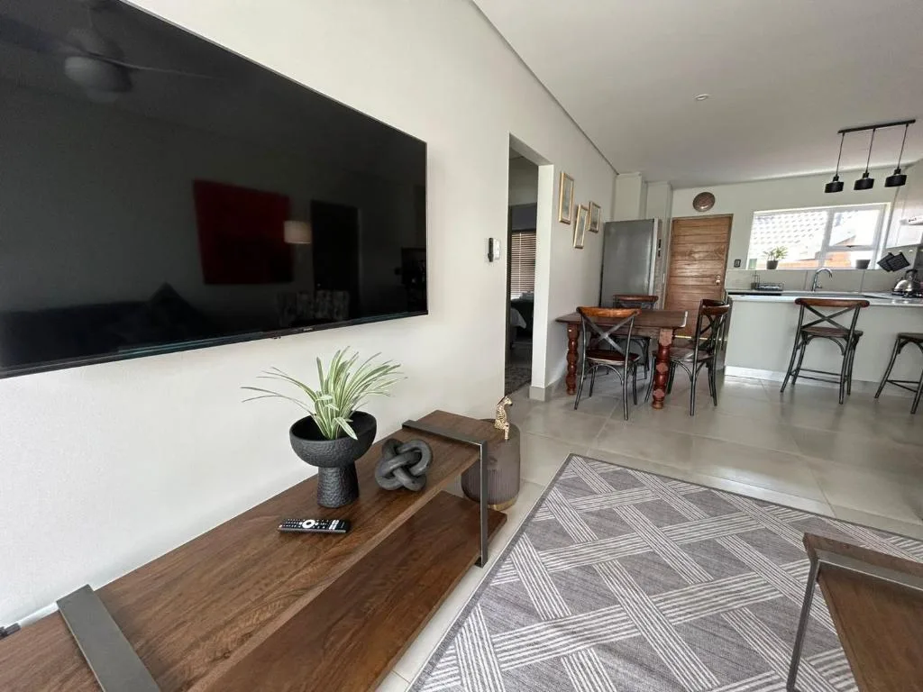 Modern lounge with wall-mounted TV, wooden console, and open-plan kitchen view