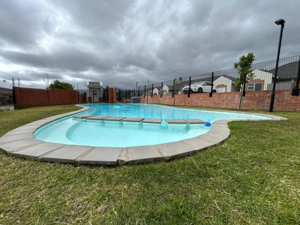 Large turquoise swimming pool with sun loungers on paved deck surrounded by green lawn