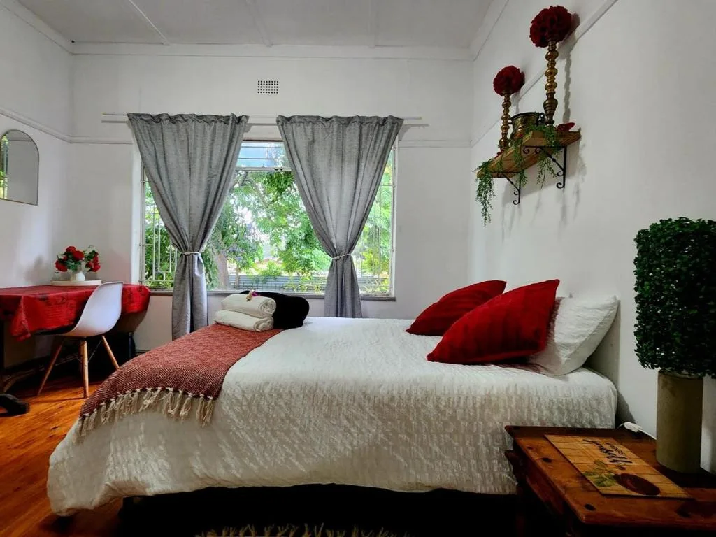 Bright bedroom with queen bed, red pillows, garden views through large windows