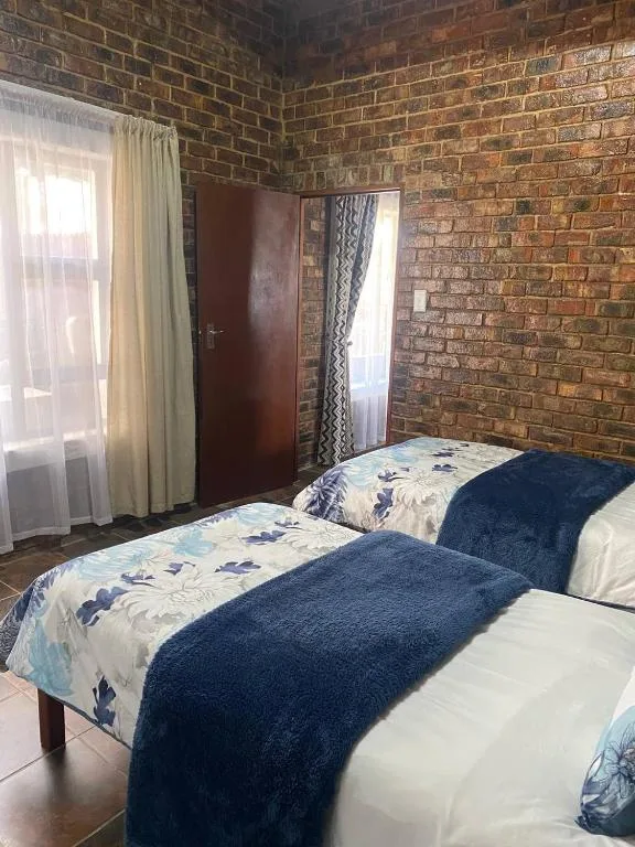 Twin beds with blue throws in brick-walled bedroom with window