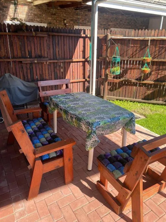 Outdoor patio with wooden furniture, table, and green lawn beyond fence