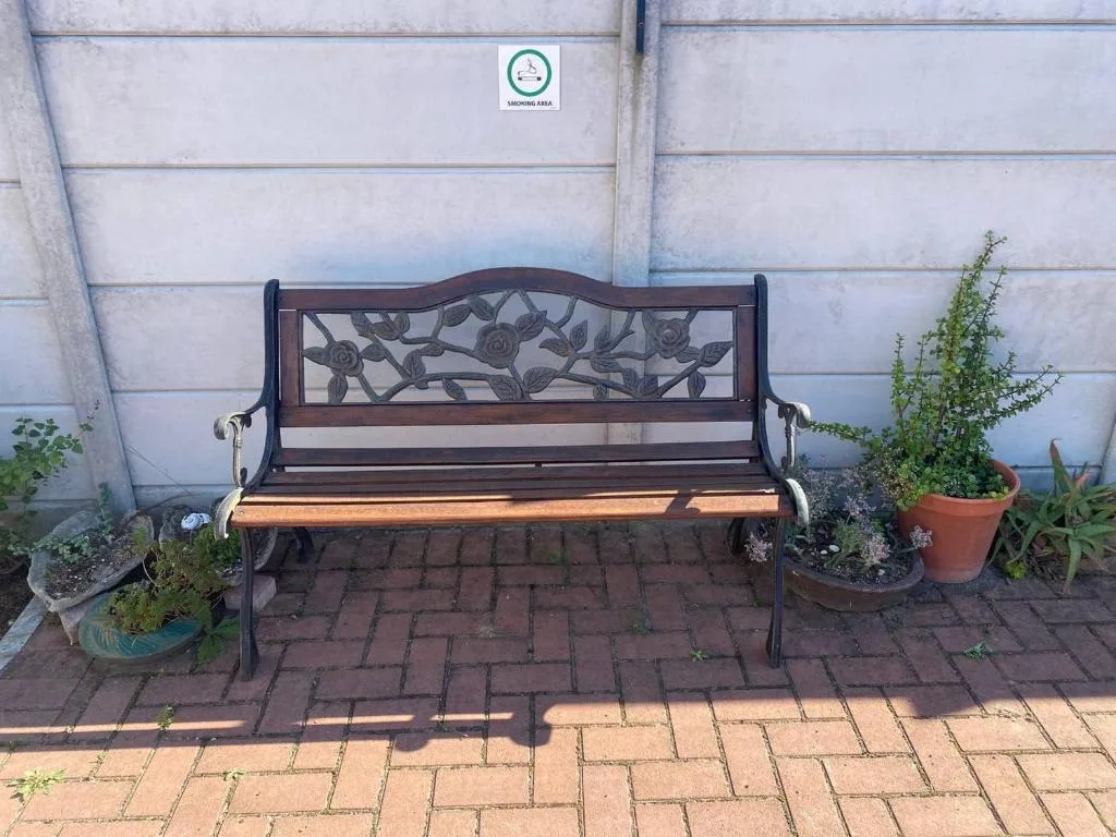 Decorative wrought iron garden bench with wooden seat against property wall