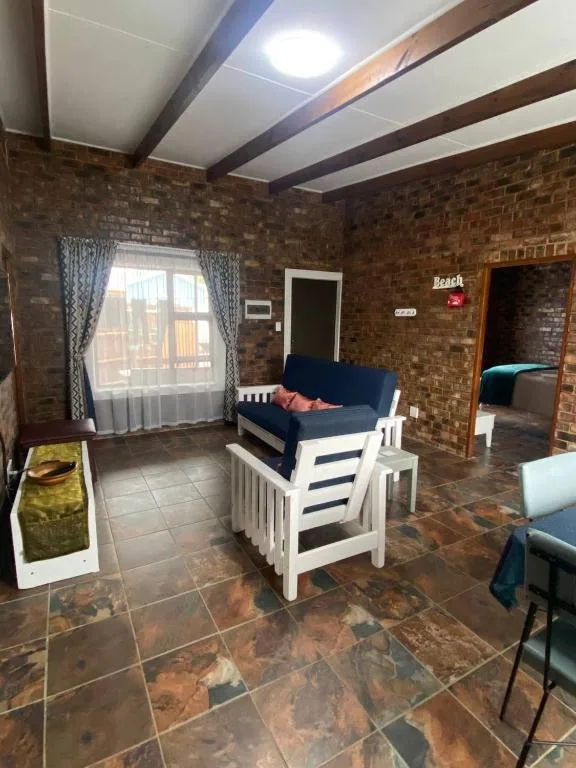 Spacious lounge with navy sofa, white armchairs, brick walls, and natural light