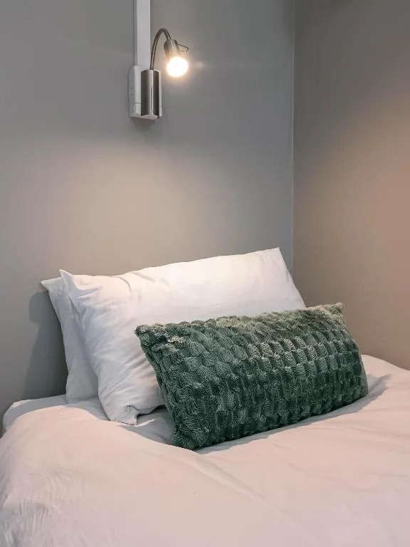 Bed with white pillows and green textured cushion under wall lamp