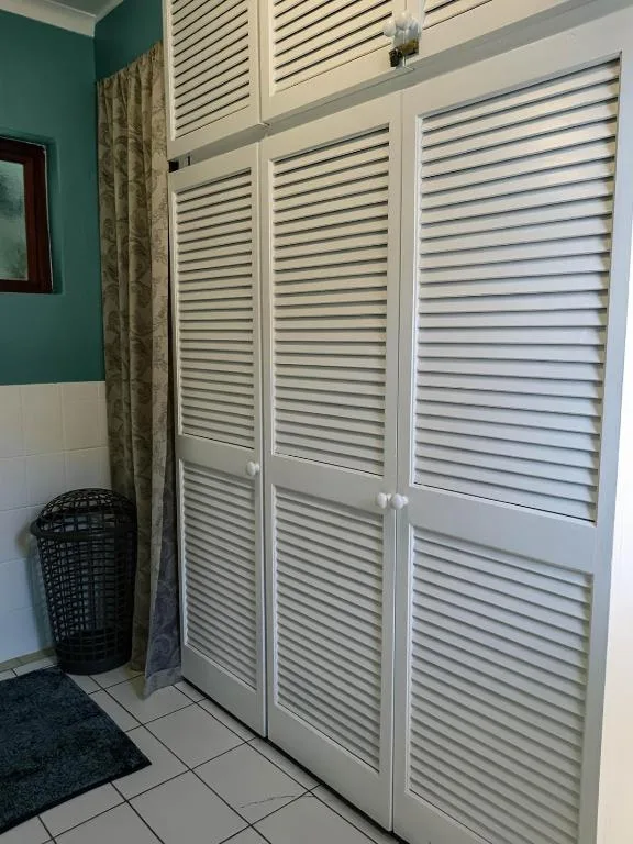 Built-in white louvered wardrobe doors with laundry basket in bedroom corner