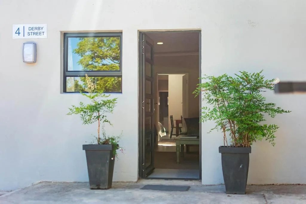 Modern white apartment entrance with dark door and potted plants