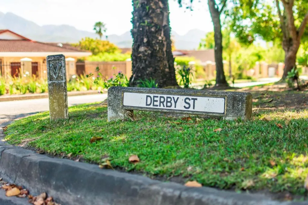 Derby Street sign with lush garden and historic building in background