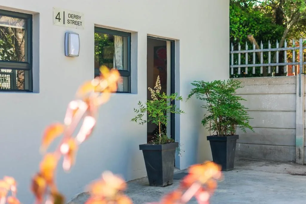 Modern white facade with Derby Street address, dark-framed doors and potted plants