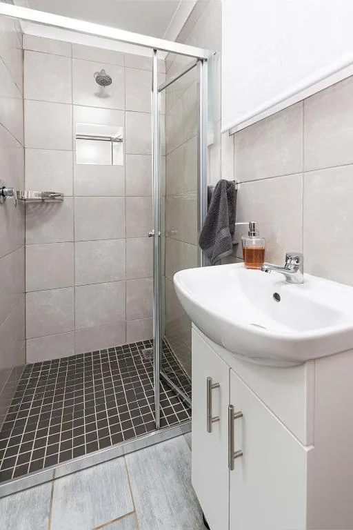 Modern bathroom with walk-in shower, white basin vanity, and dark tile flooring