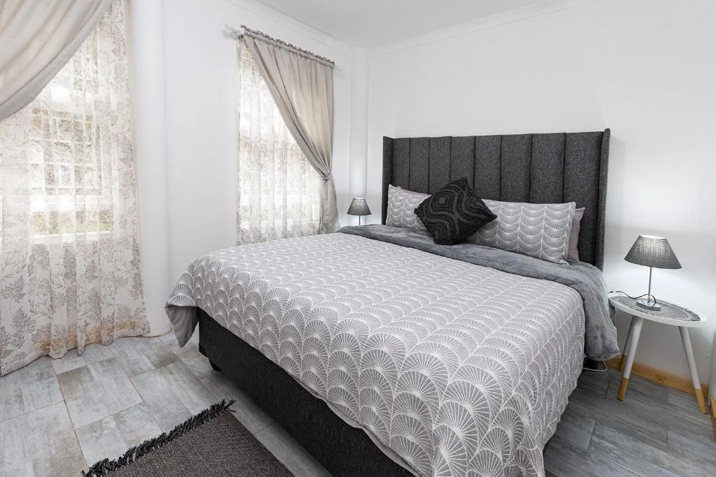 Bright bedroom with made bed, dark headboard, and large windows with curtains