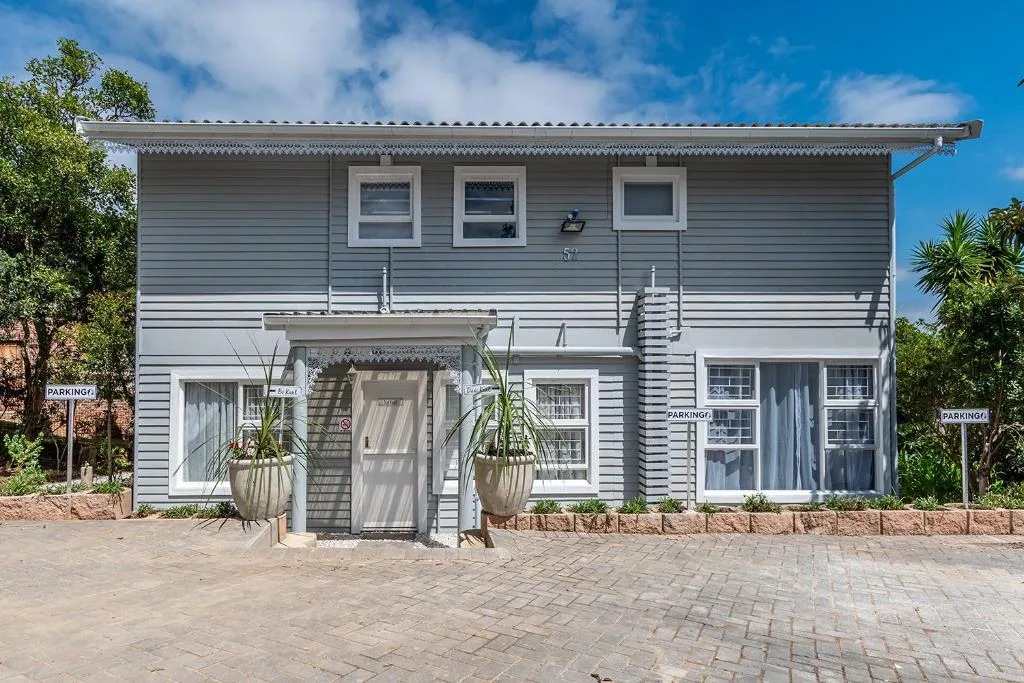 White and grey two-story cottage with parking area and potted plants