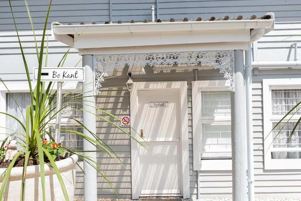 White cottage entrance with lace trim, potted plants, and signage