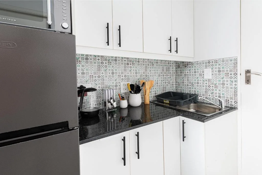 Modern kitchen with dark countertop, white cabinetry, and patterned backtile