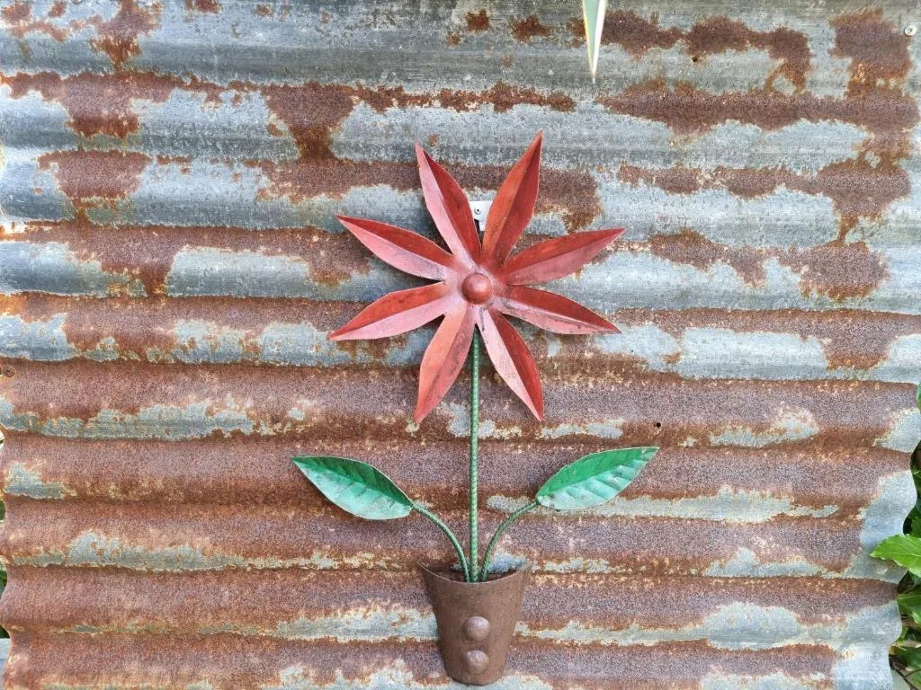 Red metal flower decoration against weathered brick wall