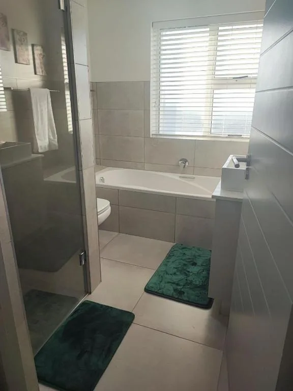 Modern bathroom with walk-in shower, bathtub, toilet, and bright windows