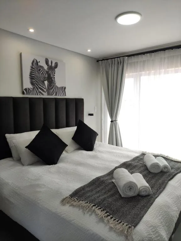 Modern bedroom with black padded headboard, white bedding, rolled towels