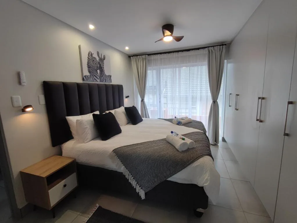 Modern bedroom with black upholstered headboard and white bedding, large windows