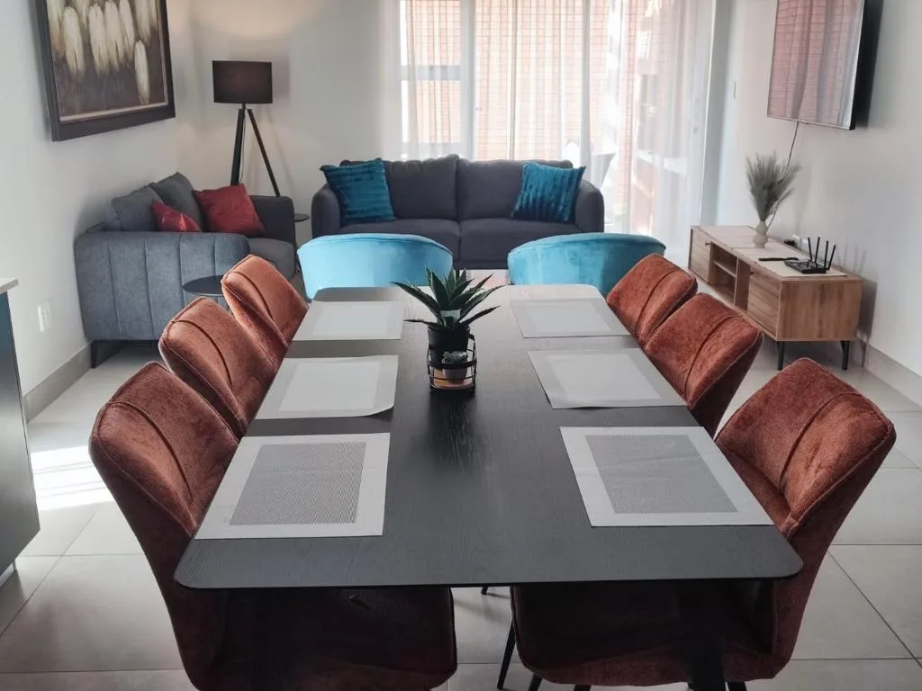 Modern dining table with burgundy chairs and place settings, lounge visible behind