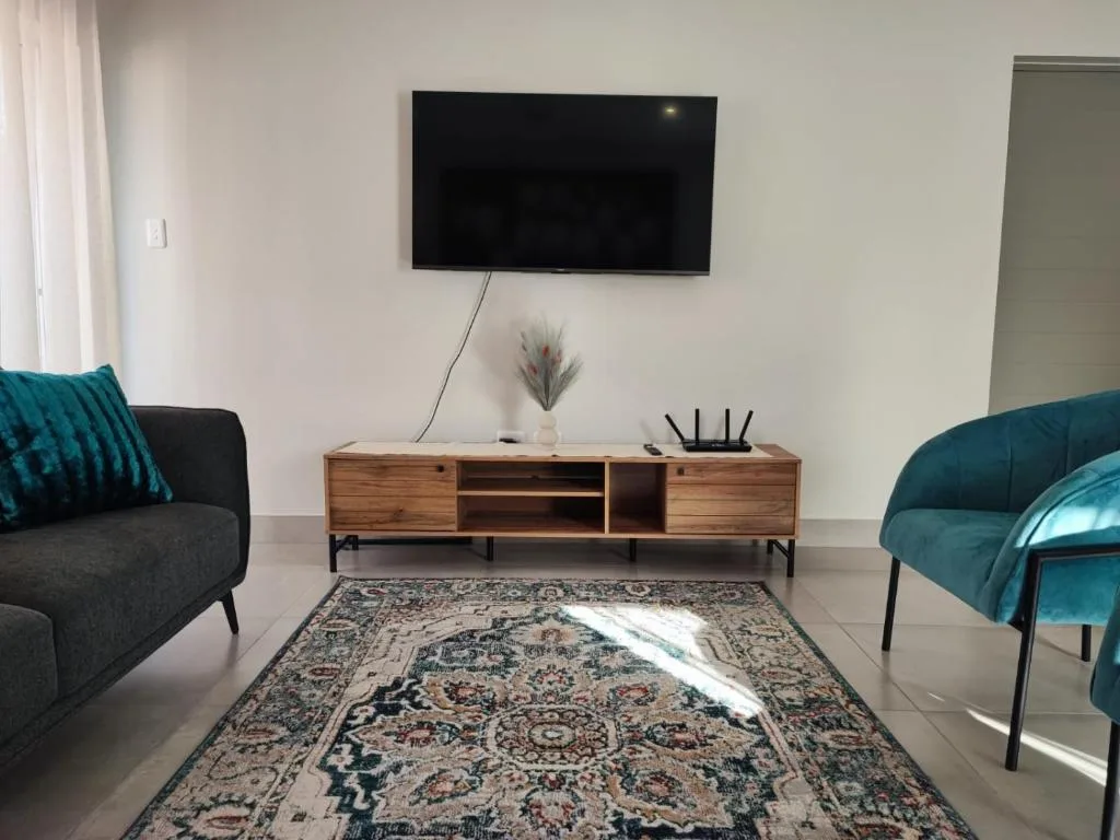 Modern lounge with teal armchairs, wall-mounted TV, and wooden media console