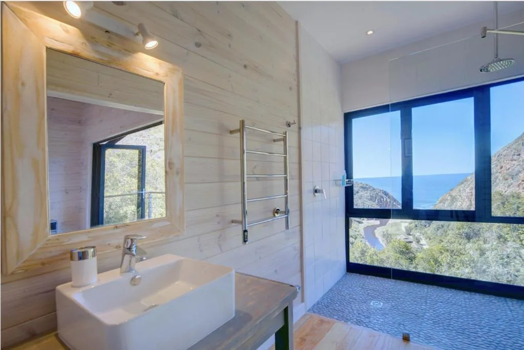 Modern bathroom with white sink, mirror, and scenic ocean mountain views through windows