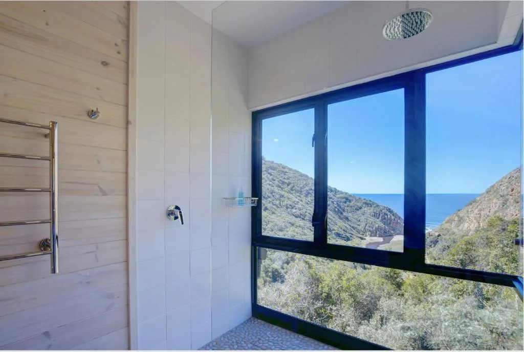 Modern bathroom with rainfall shower and expansive windows overlooking coastal mountains