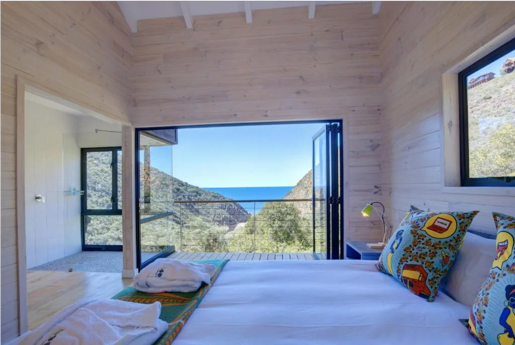 Bright bedroom with ocean view through glass doors and mountain scenery
