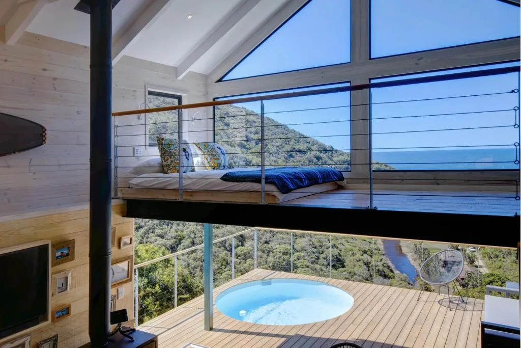 Modern loft bedroom with panoramic mountain and ocean views through floor-to-ceiling windows