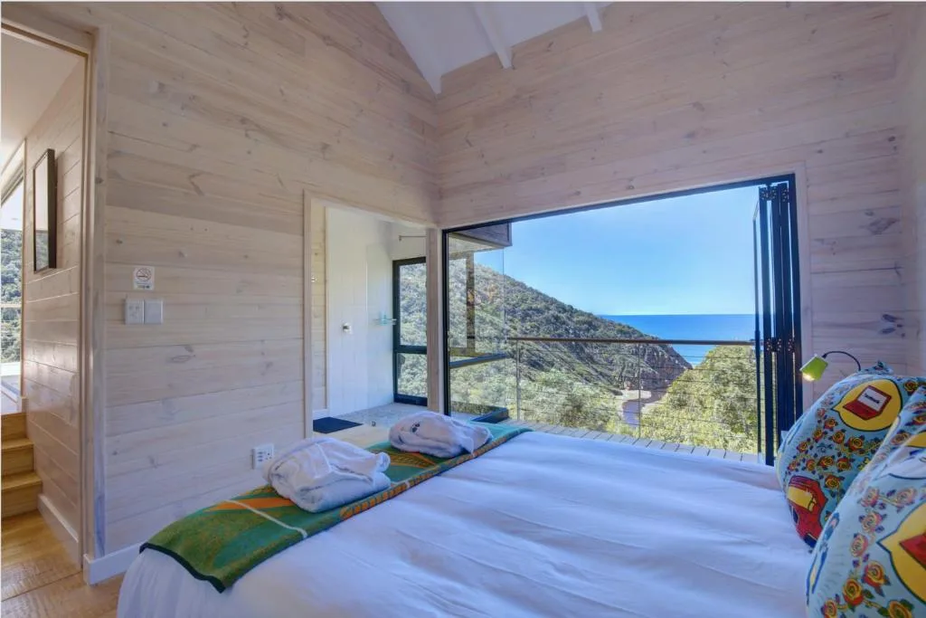 Bright bedroom with bed, wooden walls, and expansive ocean view windows