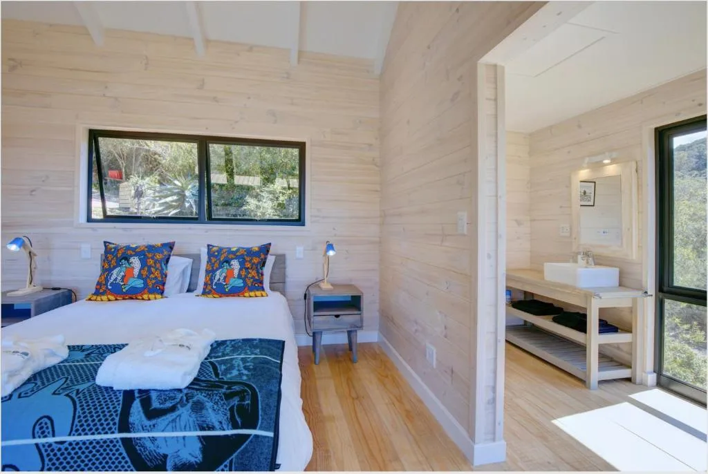 Bright bedroom with queen bed, colorful pillows, wooden walls, and en-suite bathroom visible