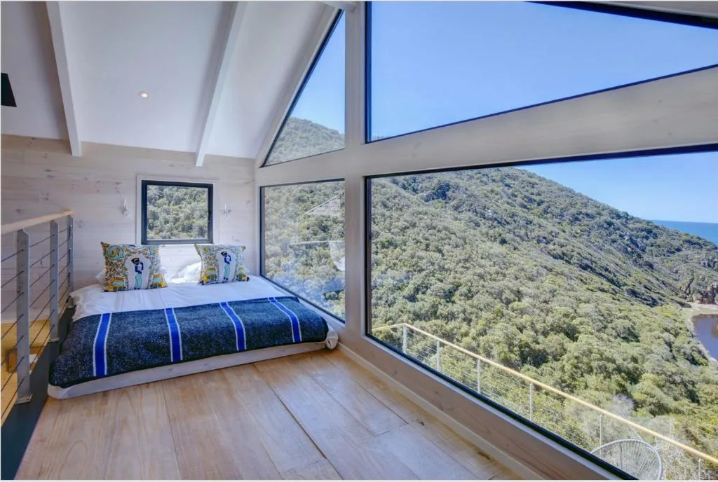 Modern bedroom with bed overlooking forested mountain and ocean views