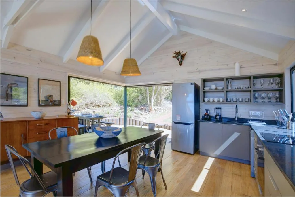 Open-plan dining area with black table, pendant lights, and kitchen beyond