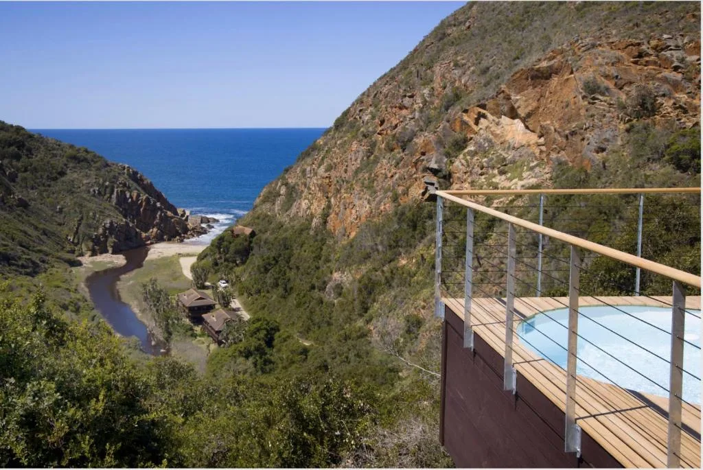 Ocean and mountain vista from wooden deck with metal railing overlooking cliffs