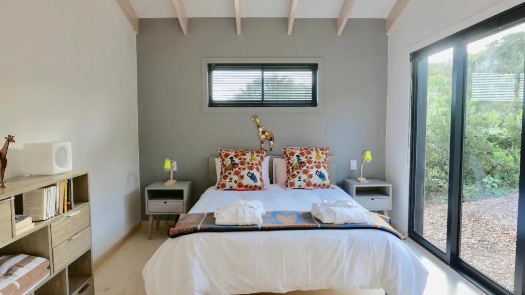 Modern bedroom with queen bed, colorful pillows, wooden furniture, and garden views