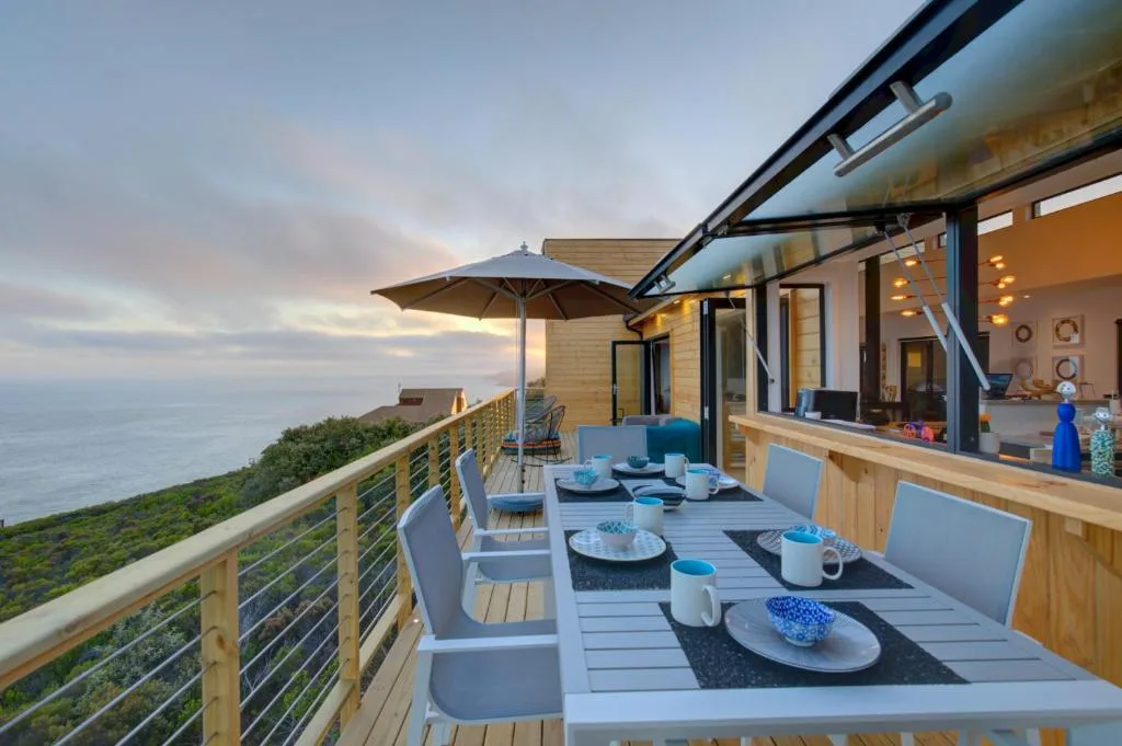 Oceanview deck with dining table, umbrella, and coastal scenery at sunset