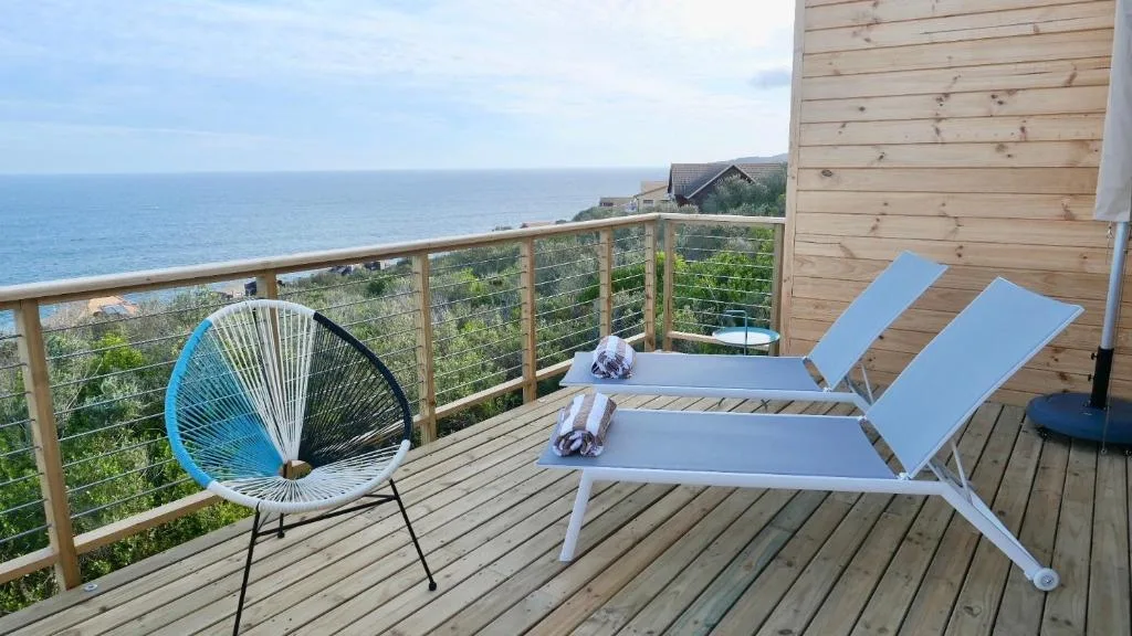Wooden deck with loungers and chair overlooking ocean coastline