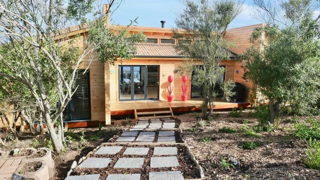 Modern wooden villa with glass doors, surrounded by native trees and plants
