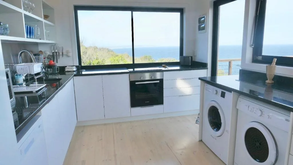 Modern white kitchen with black countertops and ocean view windows