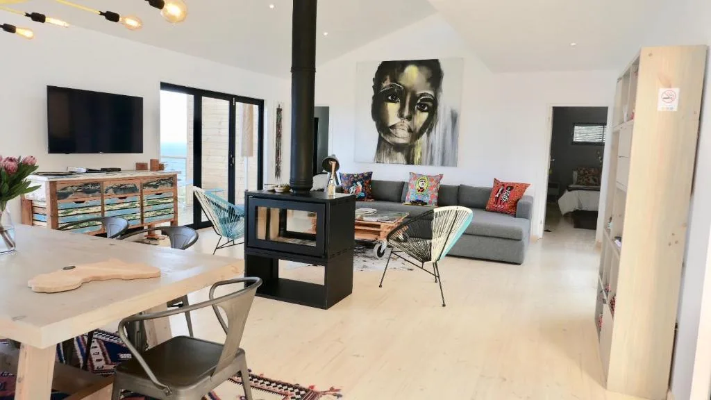 Modern open-plan lounge with fireplace, gray sofa, and ocean views through glass doors