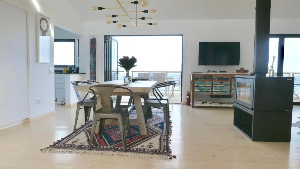 Modern open-plan living space with dining table, TV, and ocean views