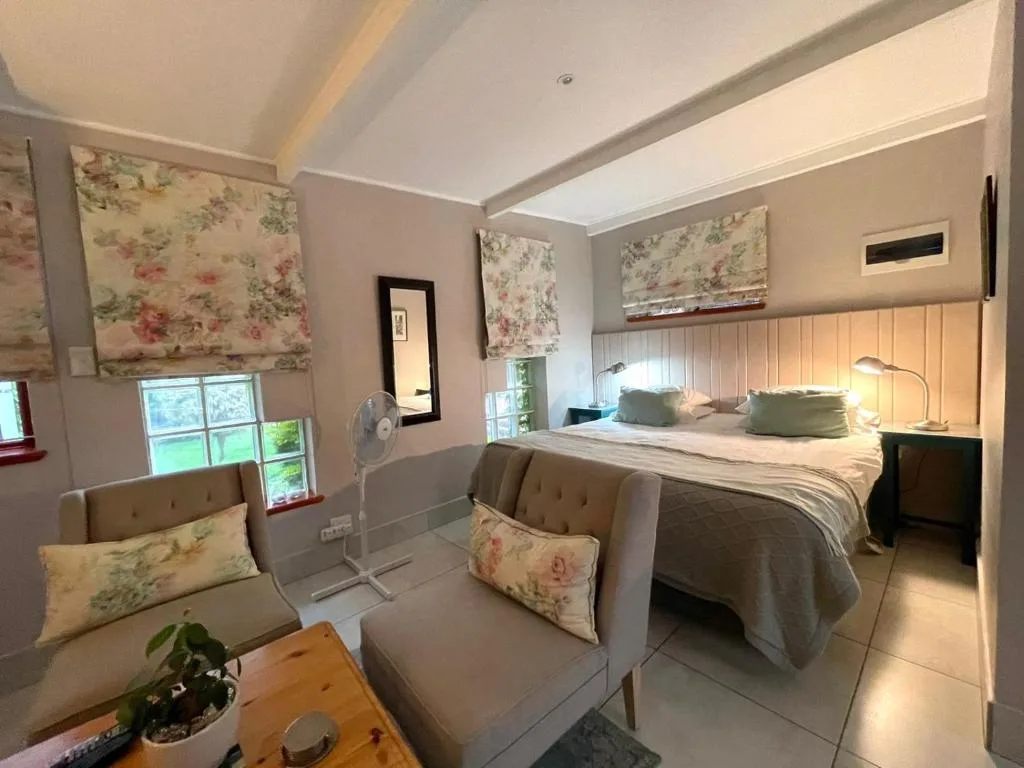 Spacious bedroom with double bed, floral roman shades, seating area, and ensuite bathroom