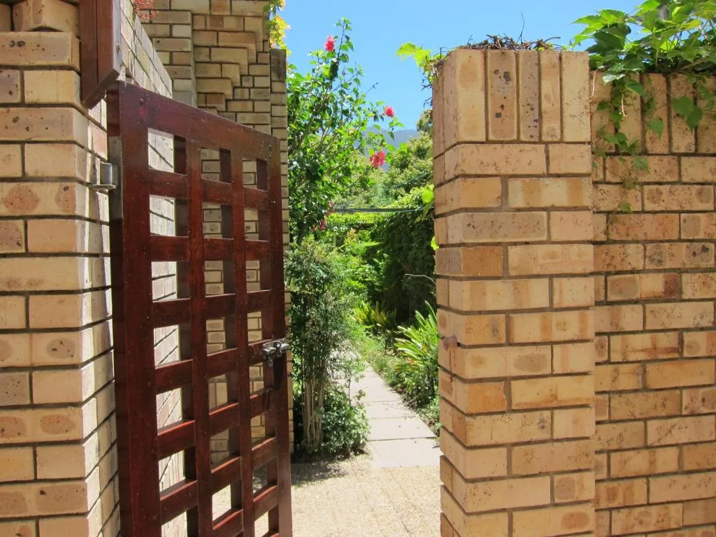 Red wooden gate and brick walls with climbing plants leading to garden path
