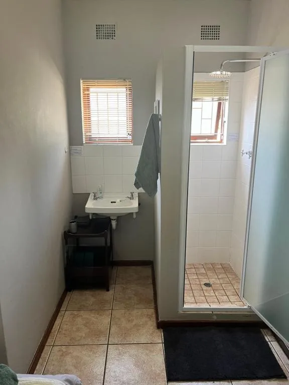 Clean bathroom with shower cubicle, pedestal sink, and tiled flooring