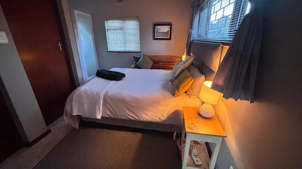 Spacious bedroom with white bedding, wooden headboard, and warm lighting from bedside lamp
