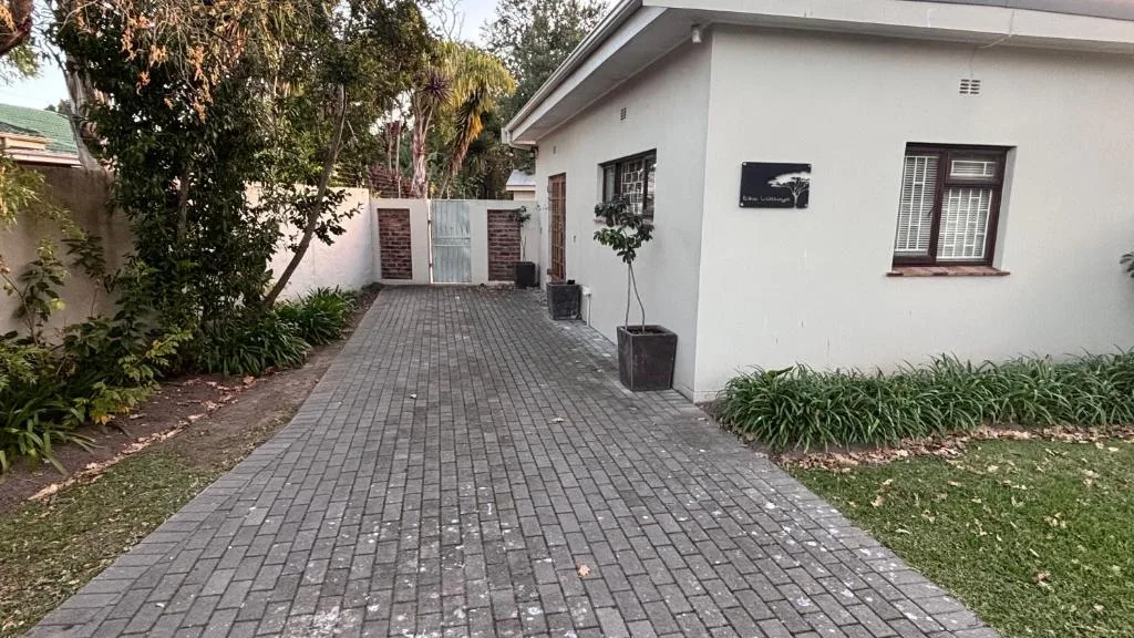 White cottage with paved driveway, garden walls, and lush landscaping